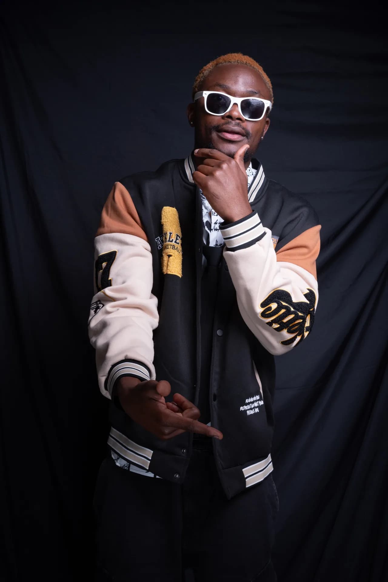 Mann in College-Jacke mit weißer Sonnenbrille im Studio