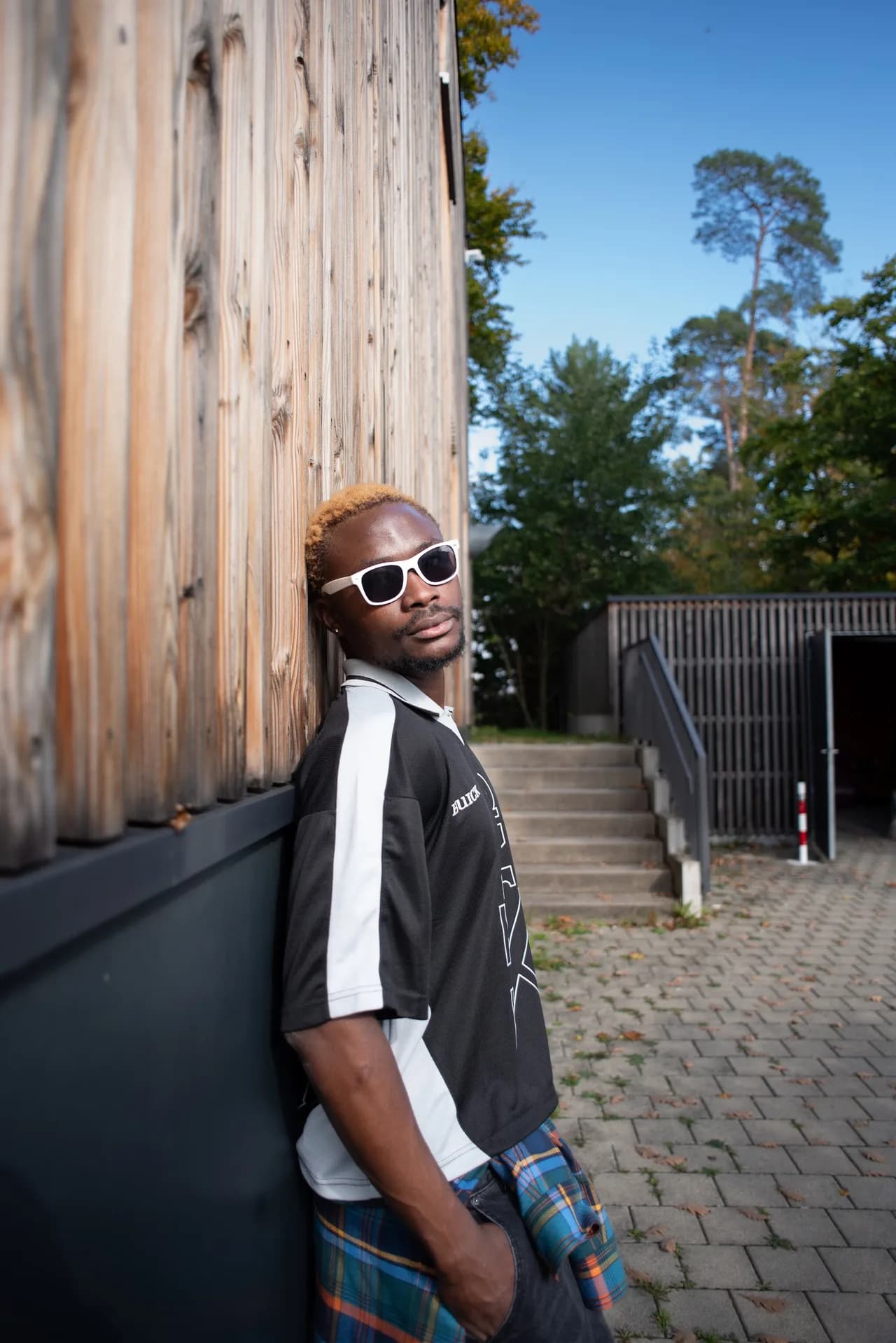Mann mit weißer Sonnenbrille lehnt an einer Holzfassade